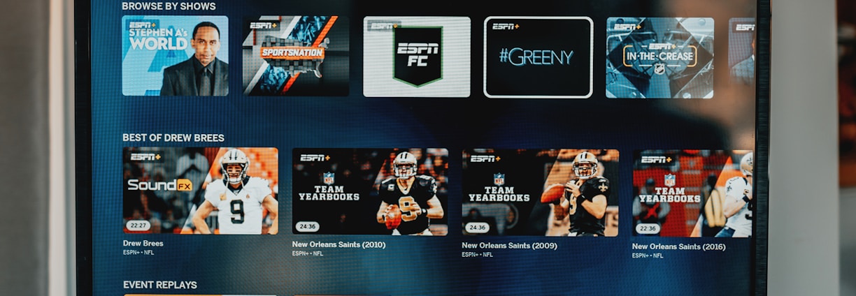 A television screen displaying the ESPN+ streaming interface with various sports-related shows and categories. The screen includes sections such as 'Browse by Shows' and 'Best of Drew Brees' with thumbnails of sports programs featuring athletes in action and analysts.